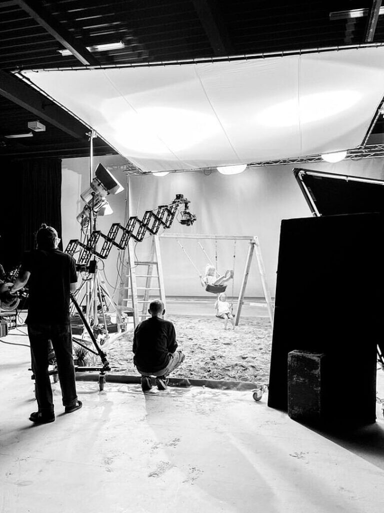 Filmset im Studio mit Kind auf Schaukel, Kamerateam und Lichttechnik bei Dreharbeiten. „Filmproduktion Studio“, „Setdesign Kinderfilm“, „Werbedreh mit Kindern“