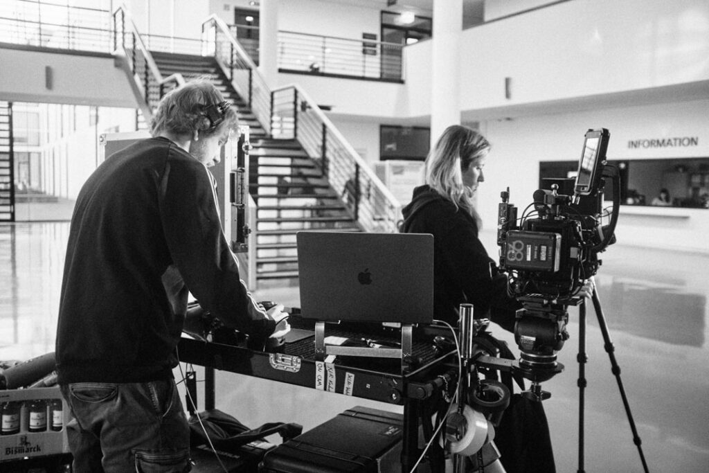 Filmteam bei Dreharbeiten in einem modernen Bürogebäude mit Kamera-, Regie- und Tontechnik im Einsatz.